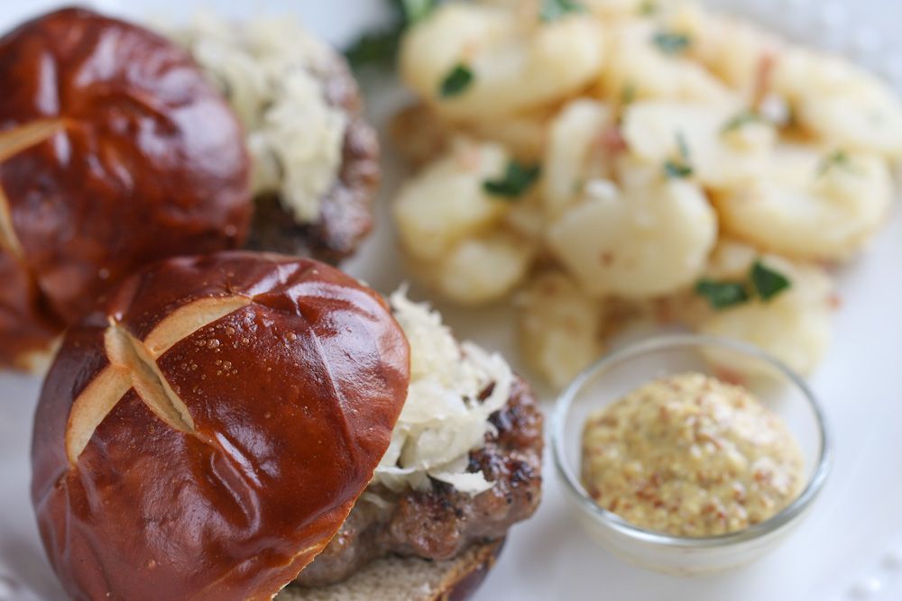 Pretzel sliders with sauerkraut, potato salad, and mustard on a plate.