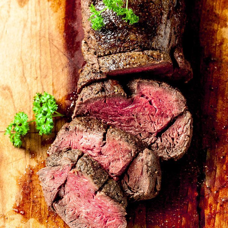 Sliced, cooked beef tenderloin on wooden cutting board with parsley garnish.