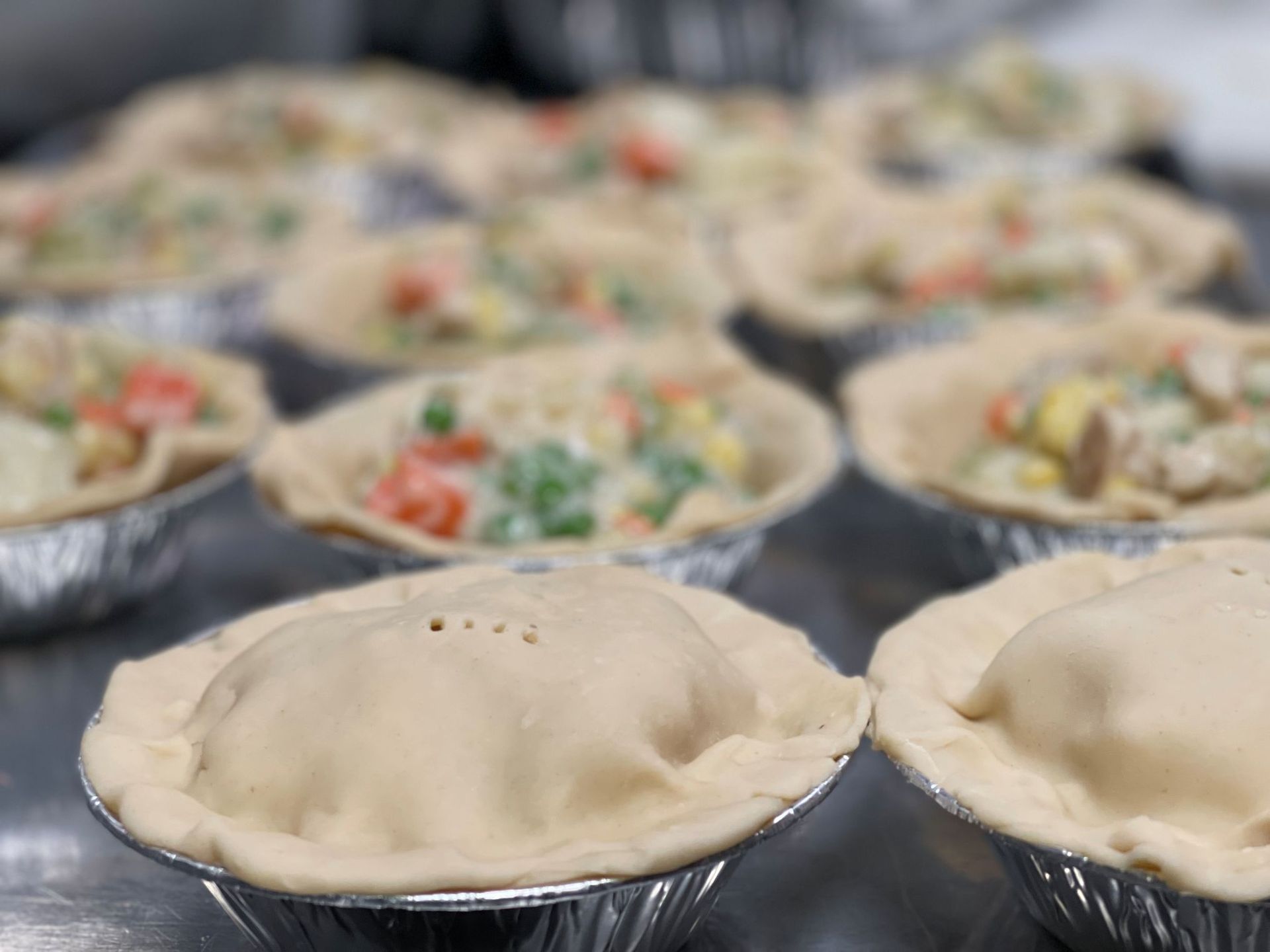 Chicken pot pies in foil tins, some with crusts, filled with vegetables and cream sauce.