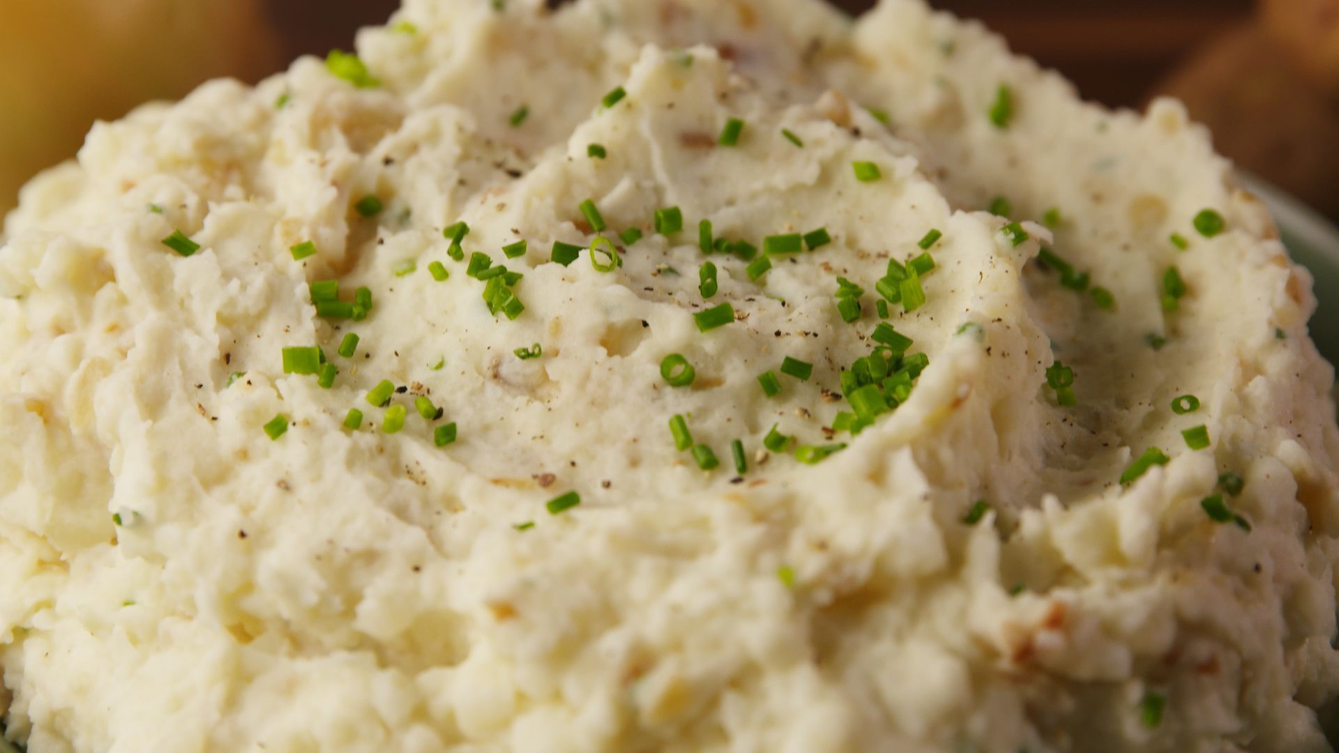 Close-up of fluffy mashed potatoes, garnished with chopped chives and black pepper.