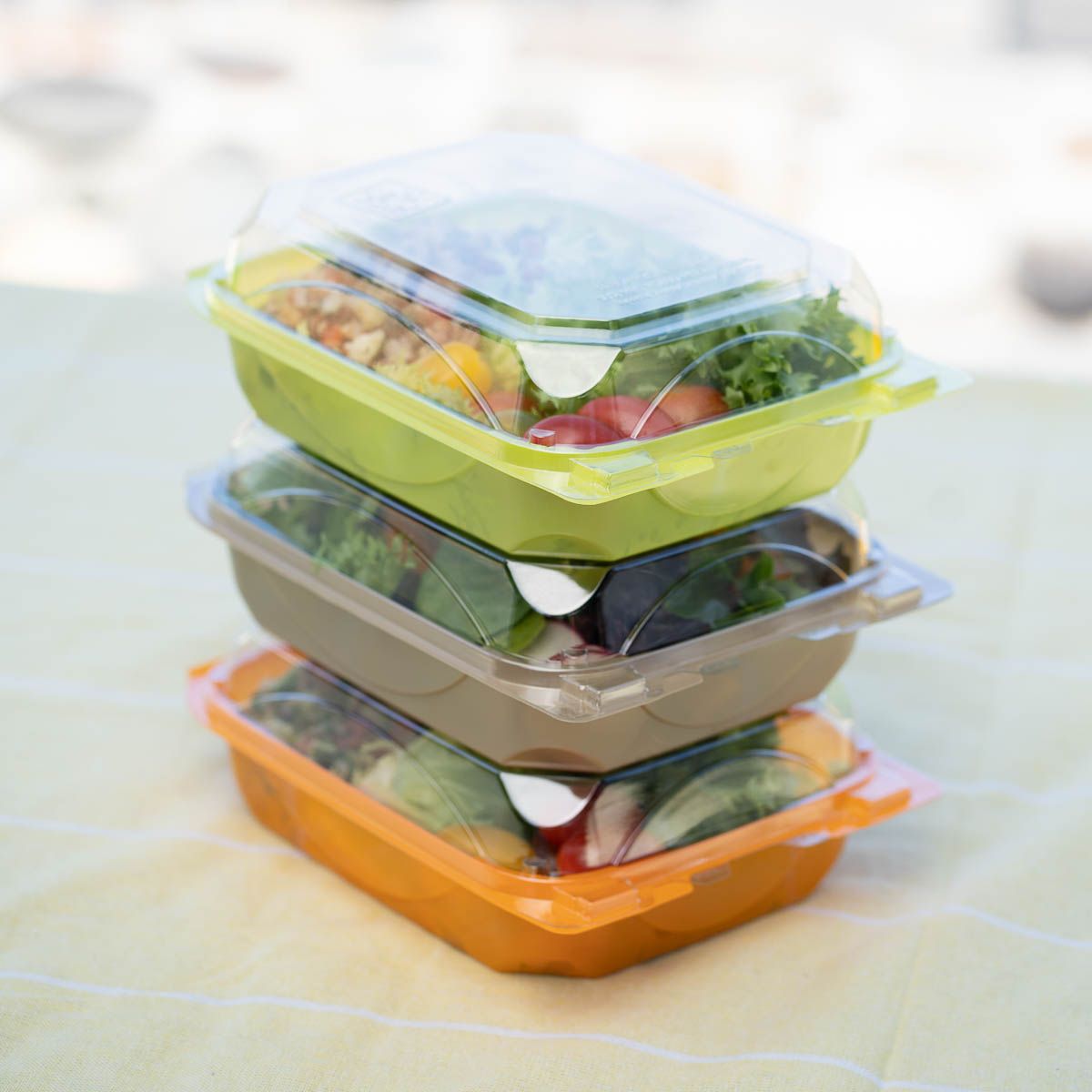 Stack of three colorful takeout containers with clear lids, each filled with salad.
