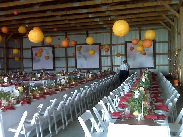 Wedding reception in a barn: long tables with white linens, red accents, decorated with flowers and lanterns.