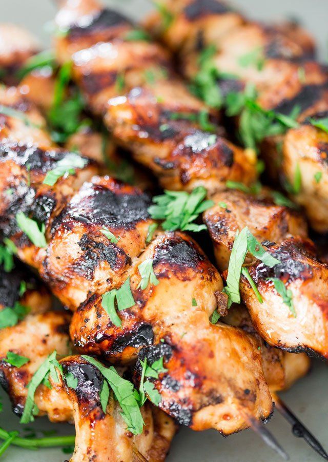 Grilled chicken skewers, charred and garnished with fresh green herbs.