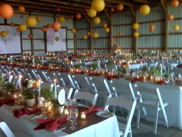 Barn wedding reception with long tables, white chairs, candles, and orange paper lanterns.