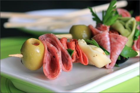Appetizer skewer with salami, olives, cheese, and herbs on a white plate.