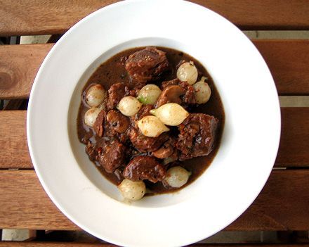 Beef bourguignon with pearl onions and mushrooms in a white bowl.