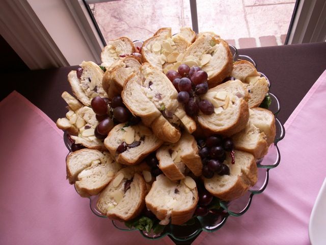 A serving dish with sliced bread rounds and grapes, on a pink tablecloth near a window.
