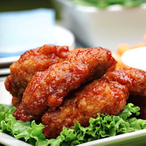 Crispy, glazed chicken wings on lettuce garnish, side of dipping sauce.