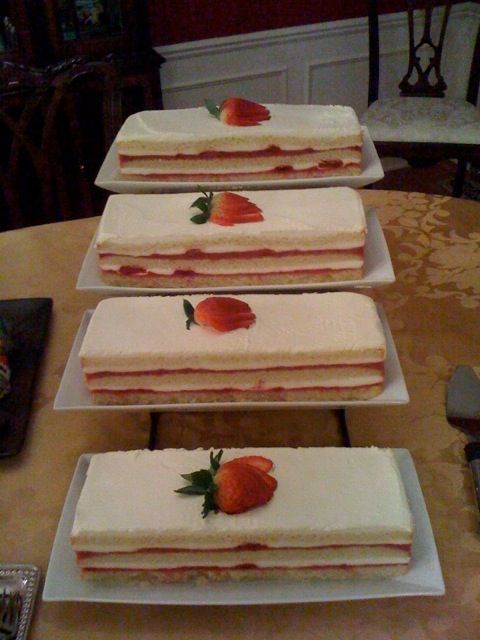 Four rectangular strawberry shortcakes stacked on a table, each topped with a strawberry and mint.