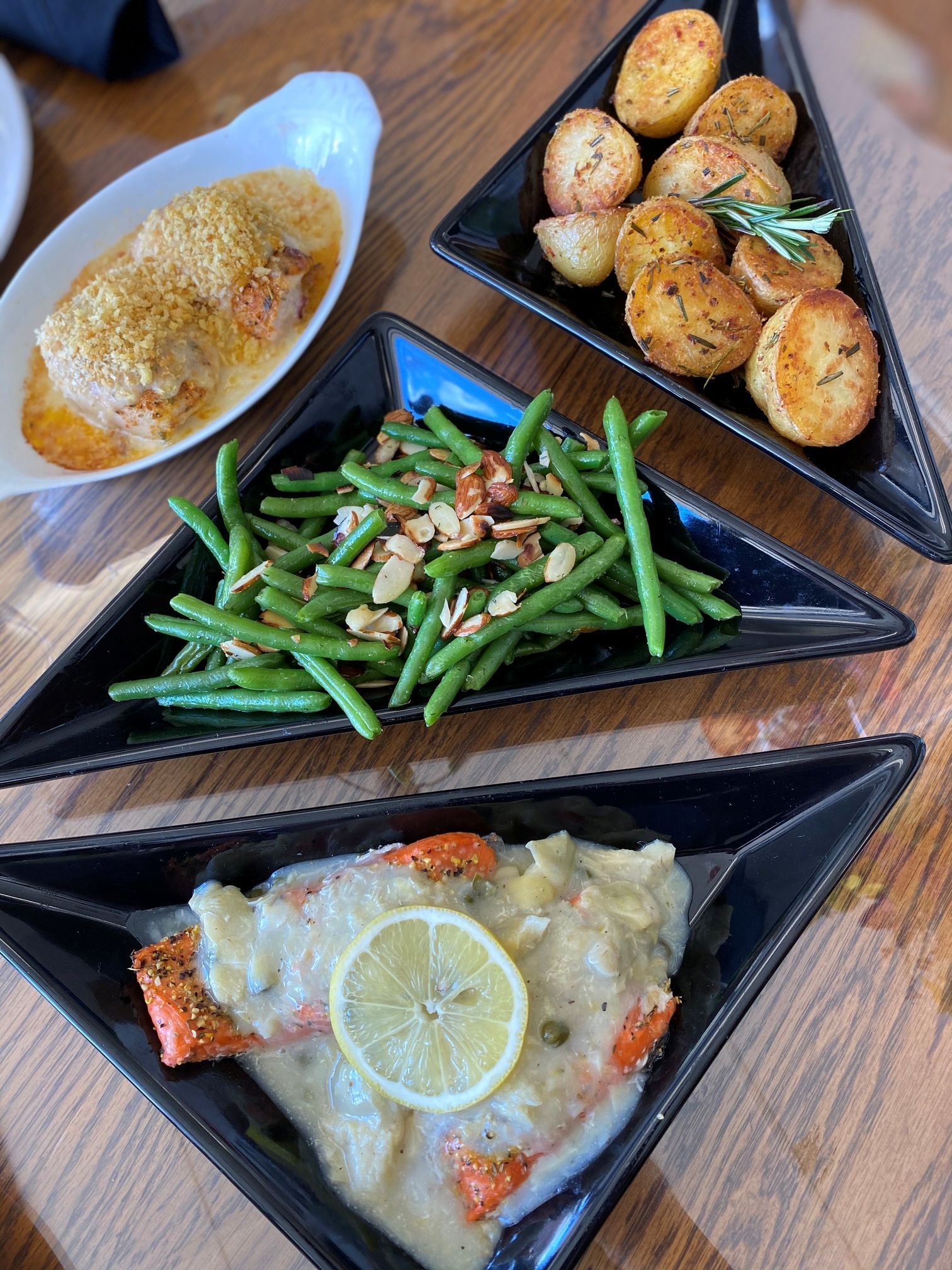 Various dishes: salmon, green beans with almonds, roasted potatoes, on black triangular plates.