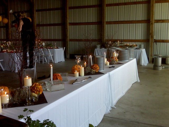 Buffet tables set for an event inside a barn, decorated with candles and flowers. A person photographs the scene.