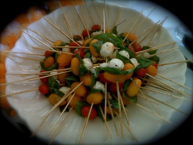 Cherry tomatoes, mozzarella balls, and basil leaves on skewers, arranged in a white bowl.