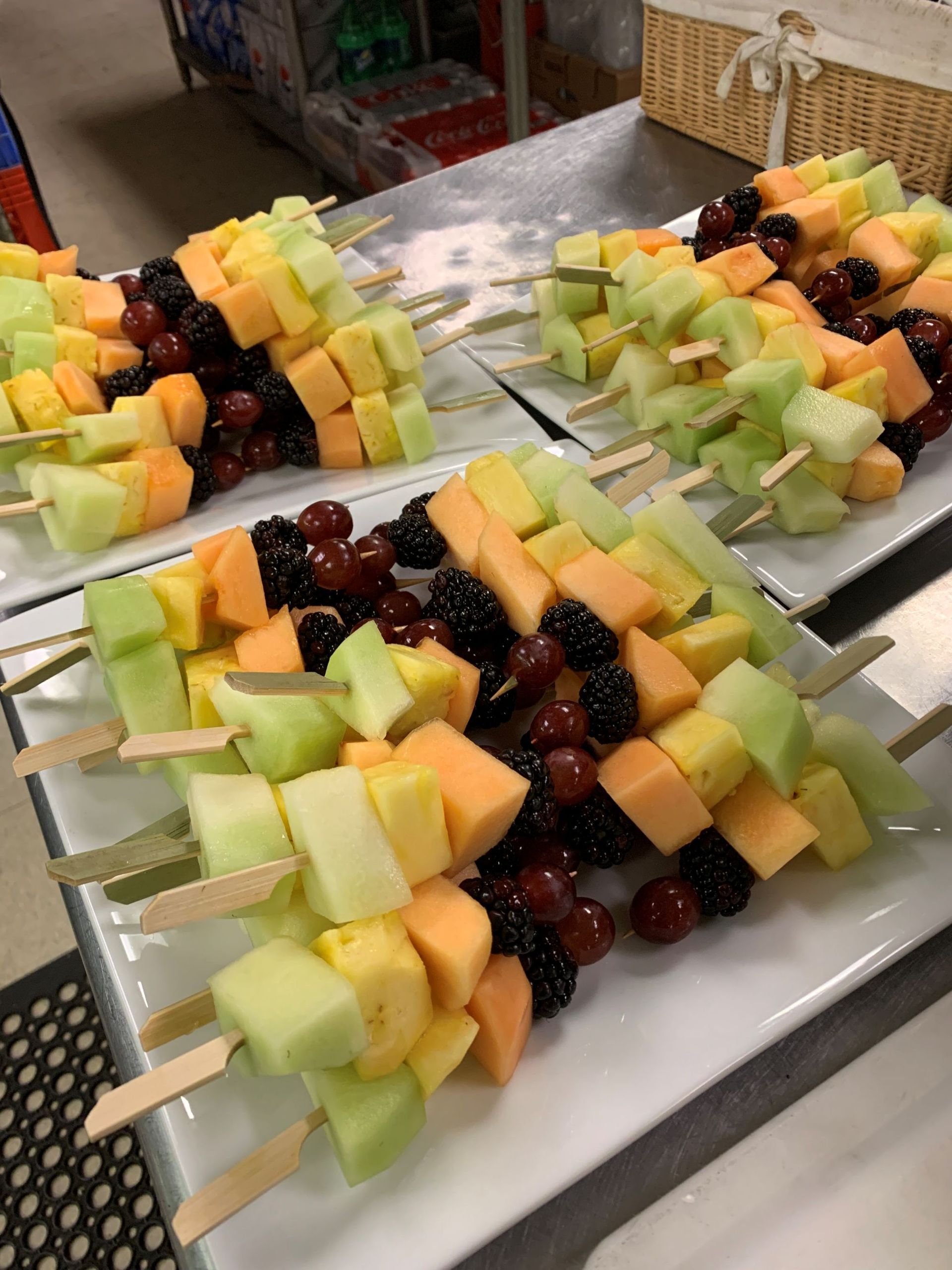 Fruit skewers: melon, pineapple, grapes, and blackberries on white plates.