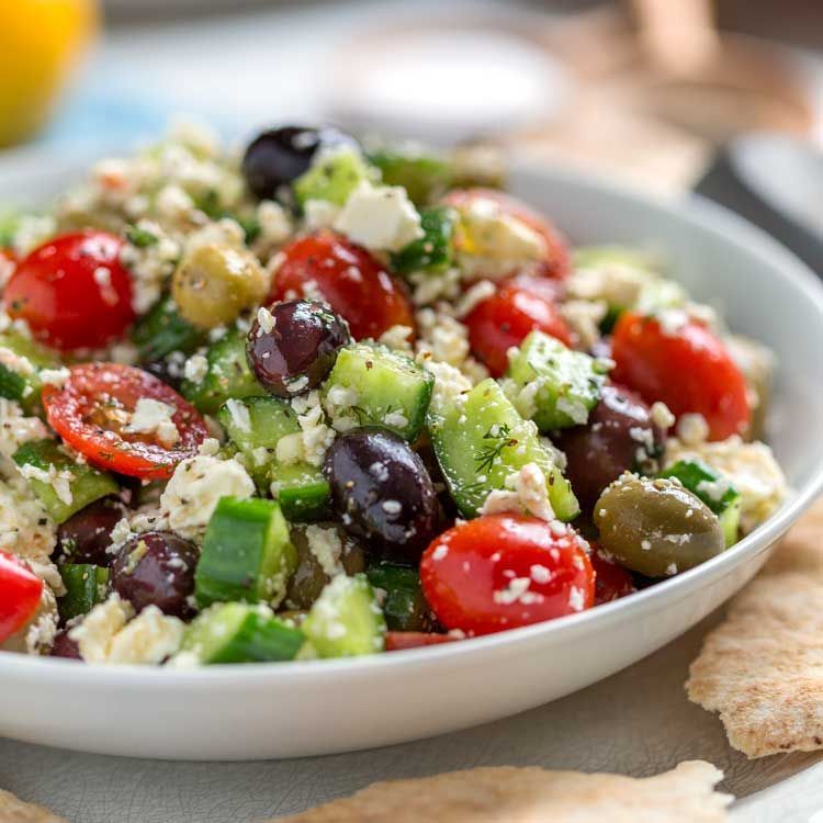 Greek salad in a white bowl: tomatoes, cucumbers, olives, feta, close-up shot.