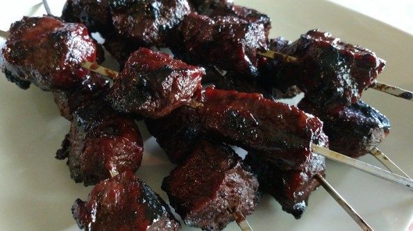 Skewered, grilled meat on a white plate; dark, glistening surface.