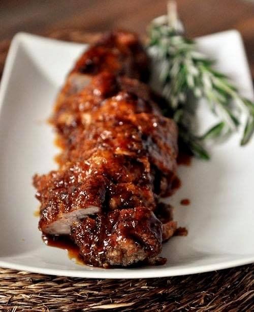 Sliced pork tenderloin with brown sauce, garnished with rosemary, on a white plate.