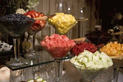 Fruit bar: blueberries, strawberries, mangoes, watermelon, raspberries, and honeydew in martini glasses on a mirrored shelf.