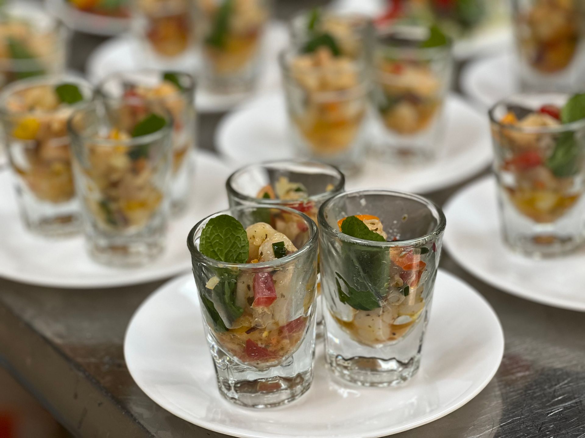 Small clear glasses filled with a colorful shrimp salad, garnished with green leaves and served on white plates.