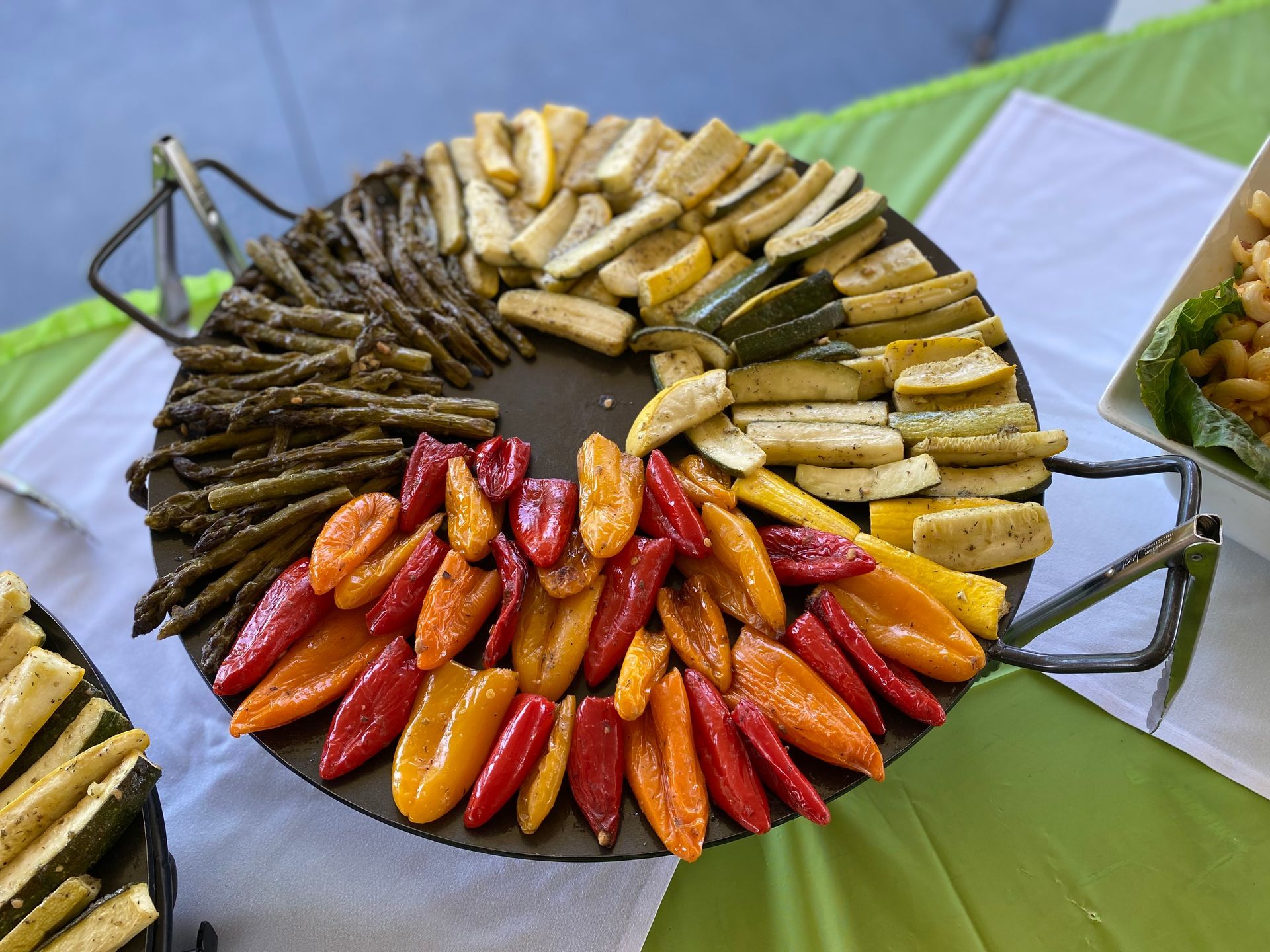 A circular platter on a table features roasted grape leaves, yellow zucchini, and colorful red and orange mini peppers.