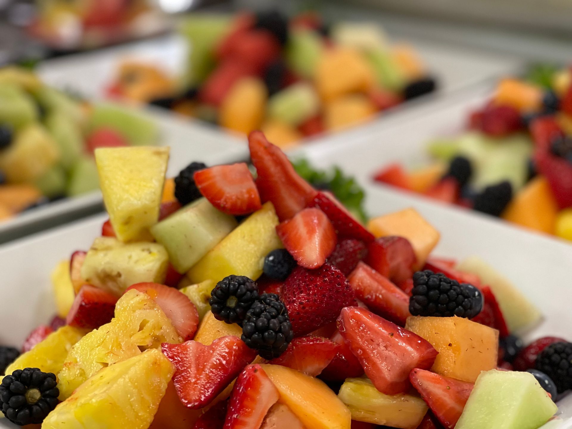 Close-up of several white bowls filled with a colorful fresh fruit salad featuring strawberries, pineapple, and berries.