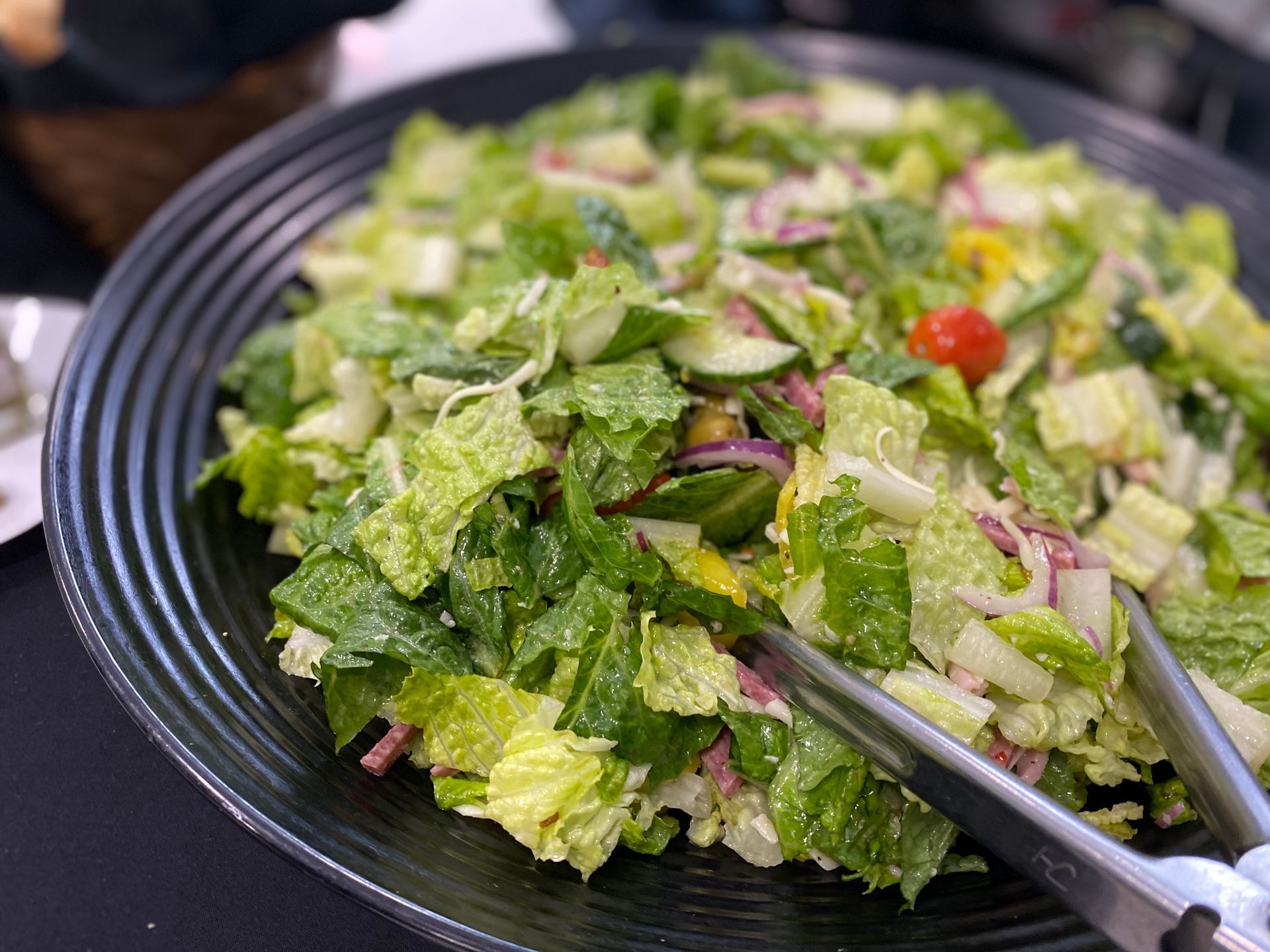 A large black bowl filled with a fresh green salad including chopped romaine, red onion, cucumber, and cherry tomatoes.
