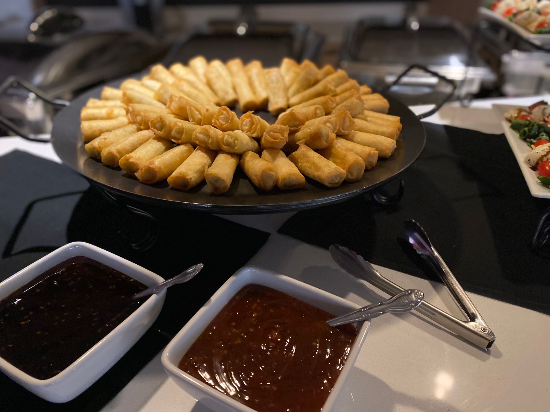 A platter of crispy fried spring rolls served with two dipping sauces on a table at a buffet.