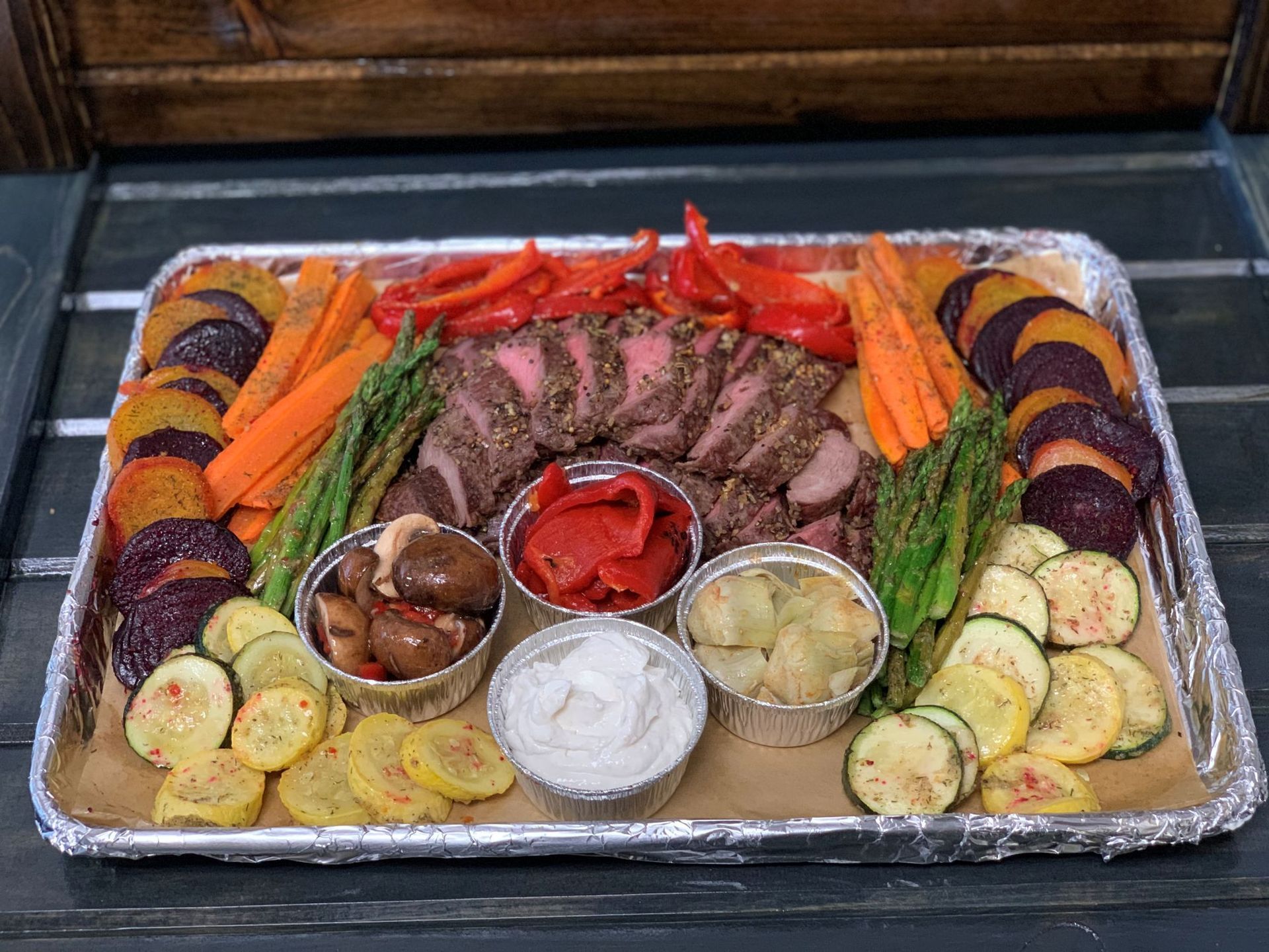 Roasted steak and vegetables arranged on a platter with dipping sauces.