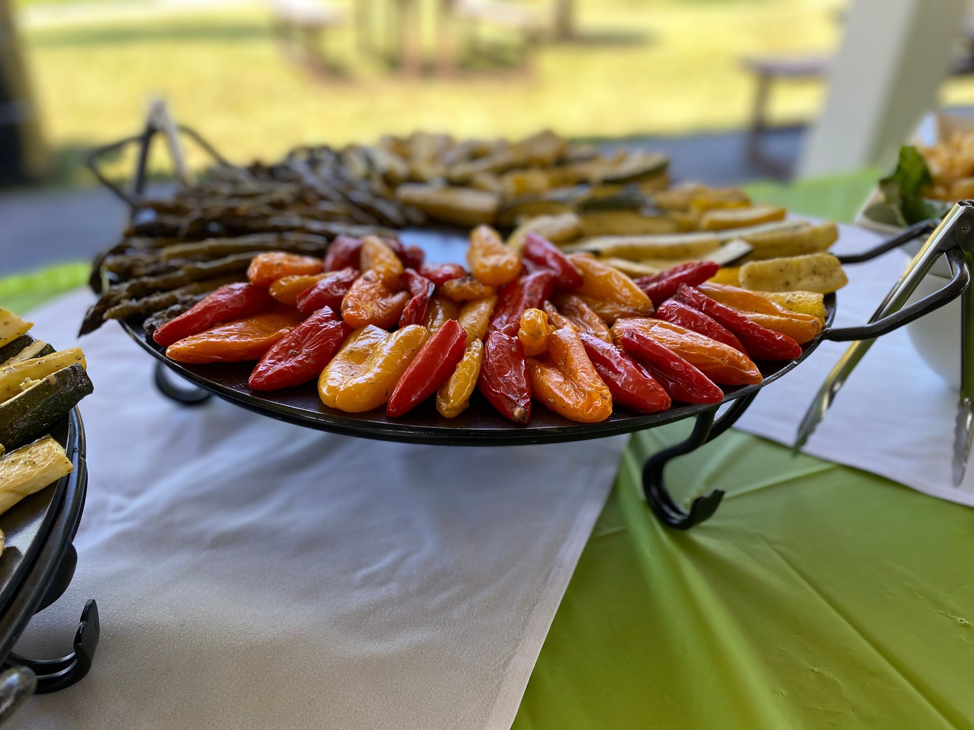 A catering platter featuring roasted asparagus, zucchini, and colorful mini sweet peppers arranged on a serving stand.