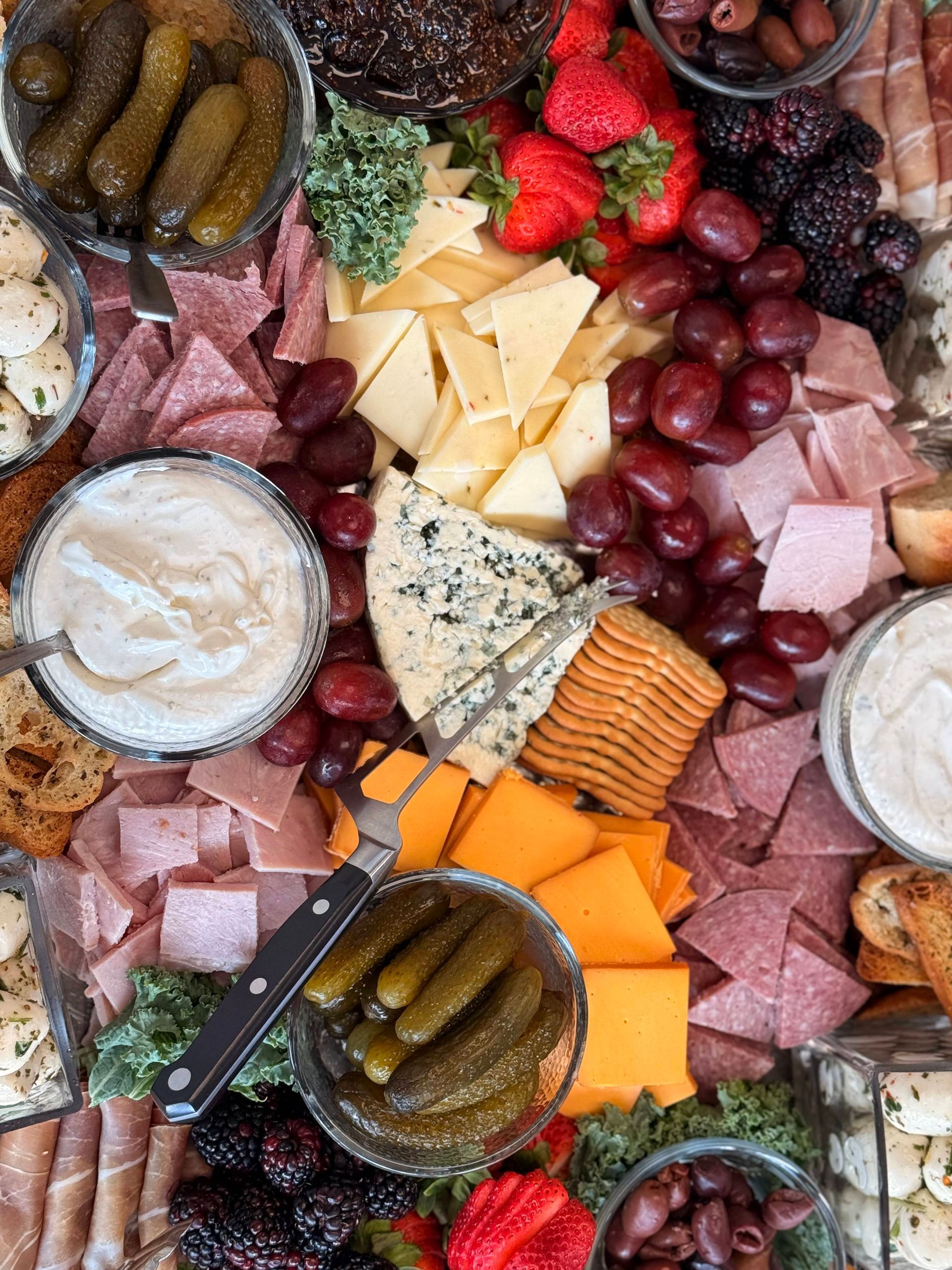 A vibrant charcuterie board filled with various meats, cheeses, crackers, pickles, fruits, and dips.
