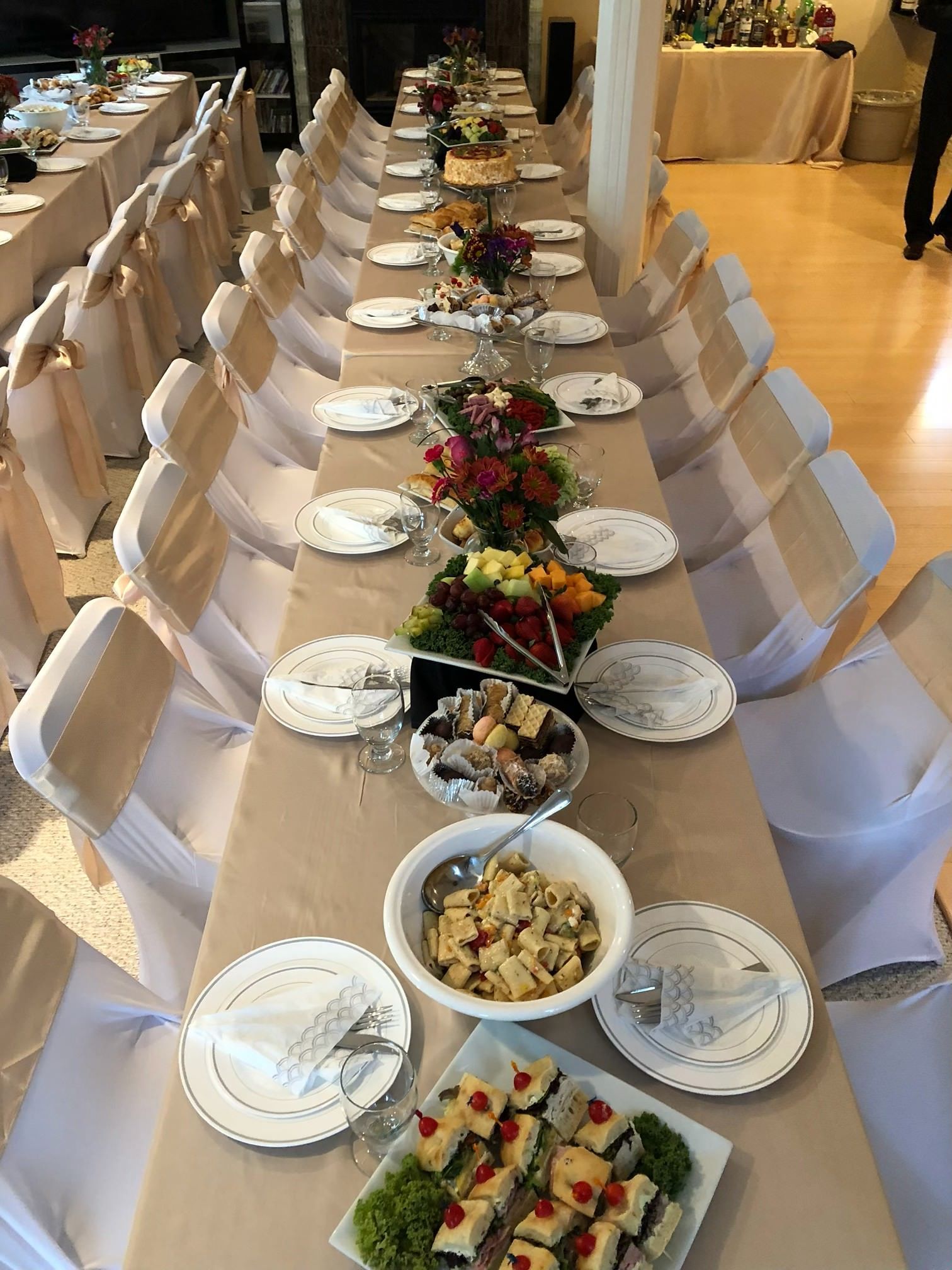 A long banquet table set for a formal event, featuring rows of white-covered chairs and platters of appetizers.