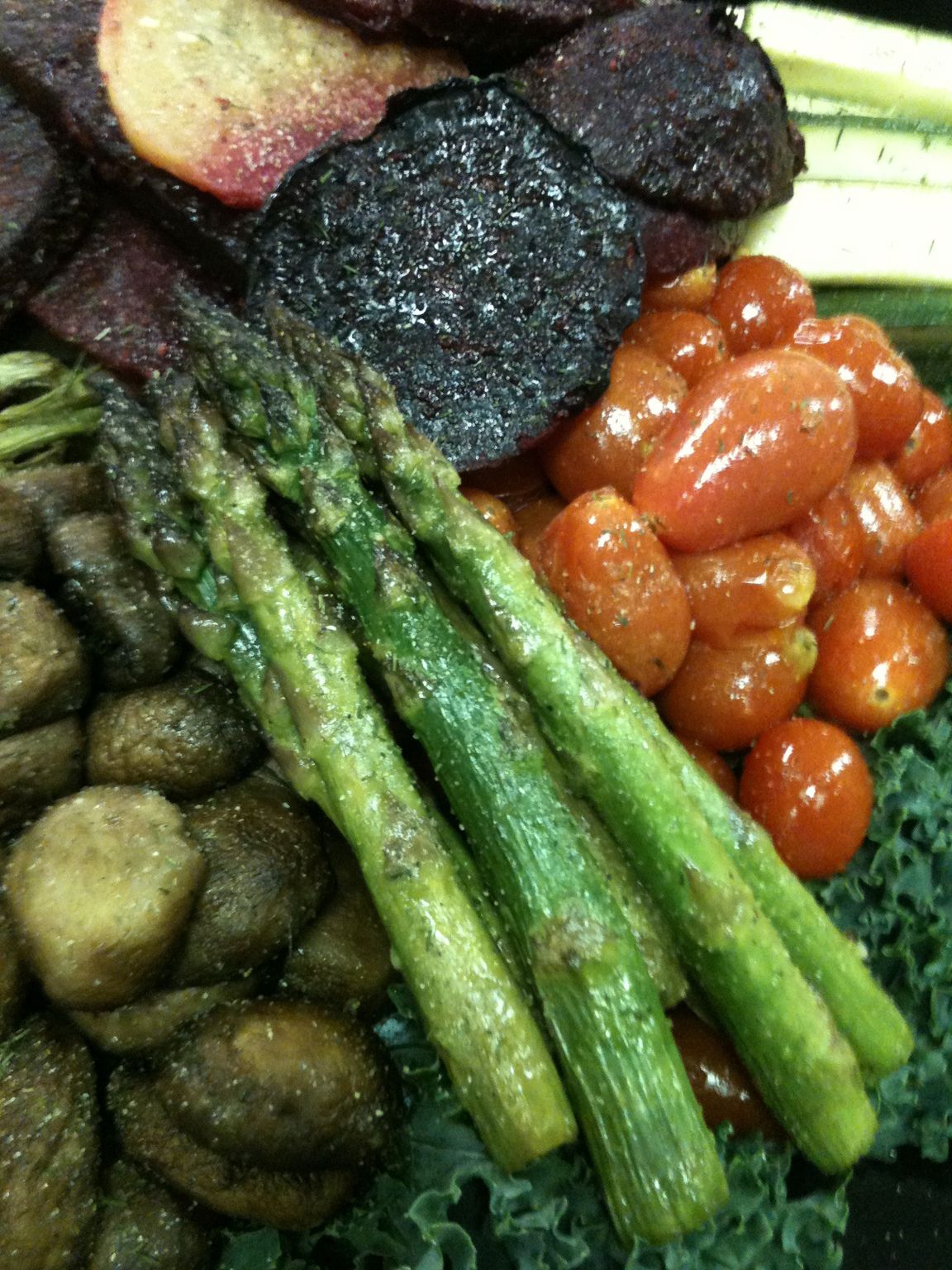 A colorful plate featuring roasted asparagus, cherry tomatoes, sliced beets, and roasted mushrooms over a bed of kale.