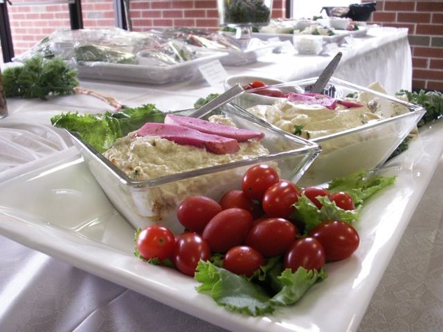 Two glass bowls of dip topped with pink slices on a white platter, garnished with fresh lettuce and cherry tomatoes.