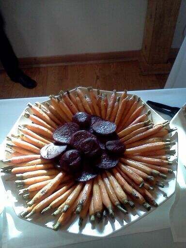A platter arranged with a ring of small, whole carrots surrounding a central pile of dark purple beet slices.