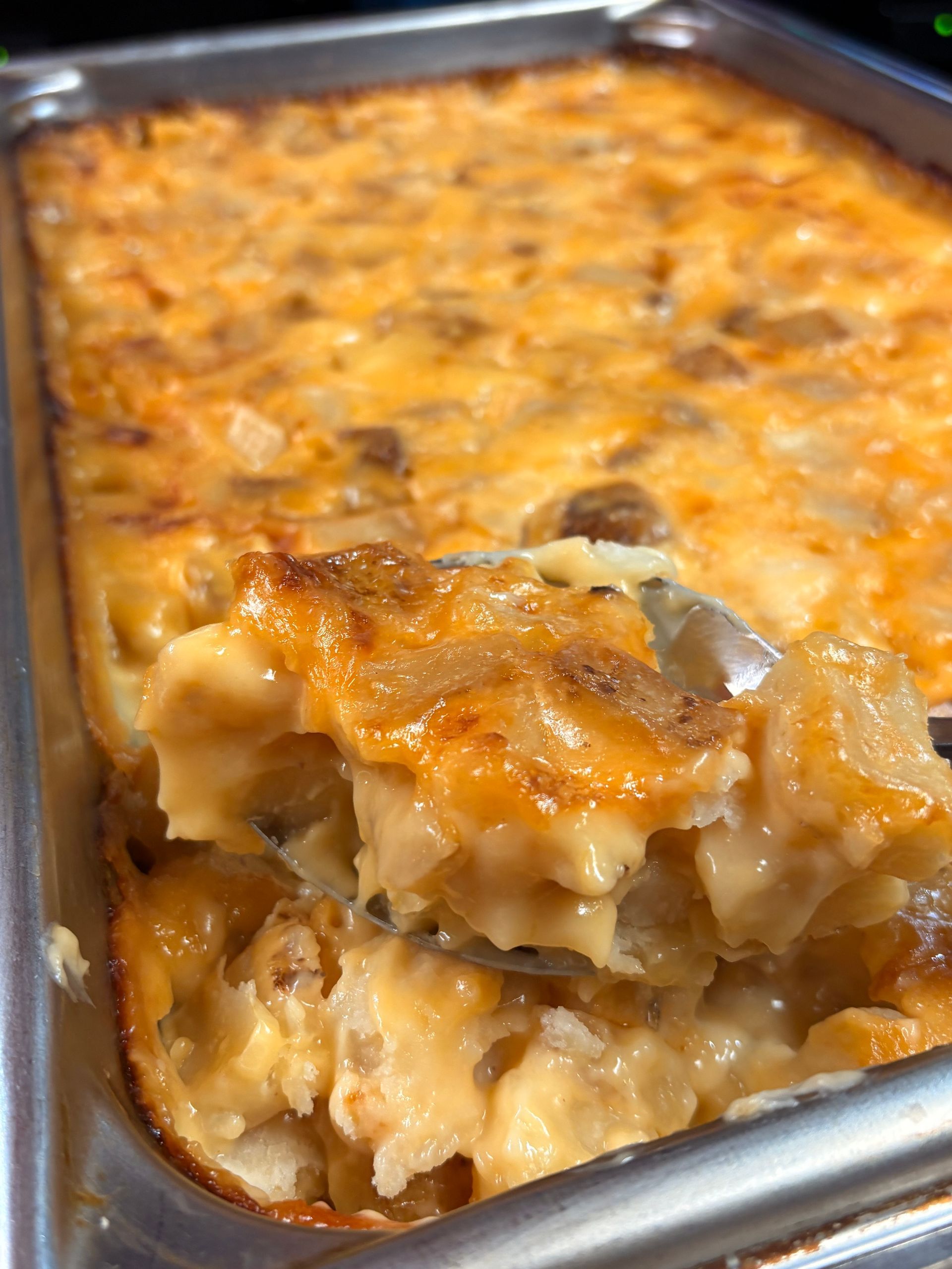 A metal pan filled with cheesy, baked potato casserole, with a large spoonful lifted to show a creamy, textured interior.