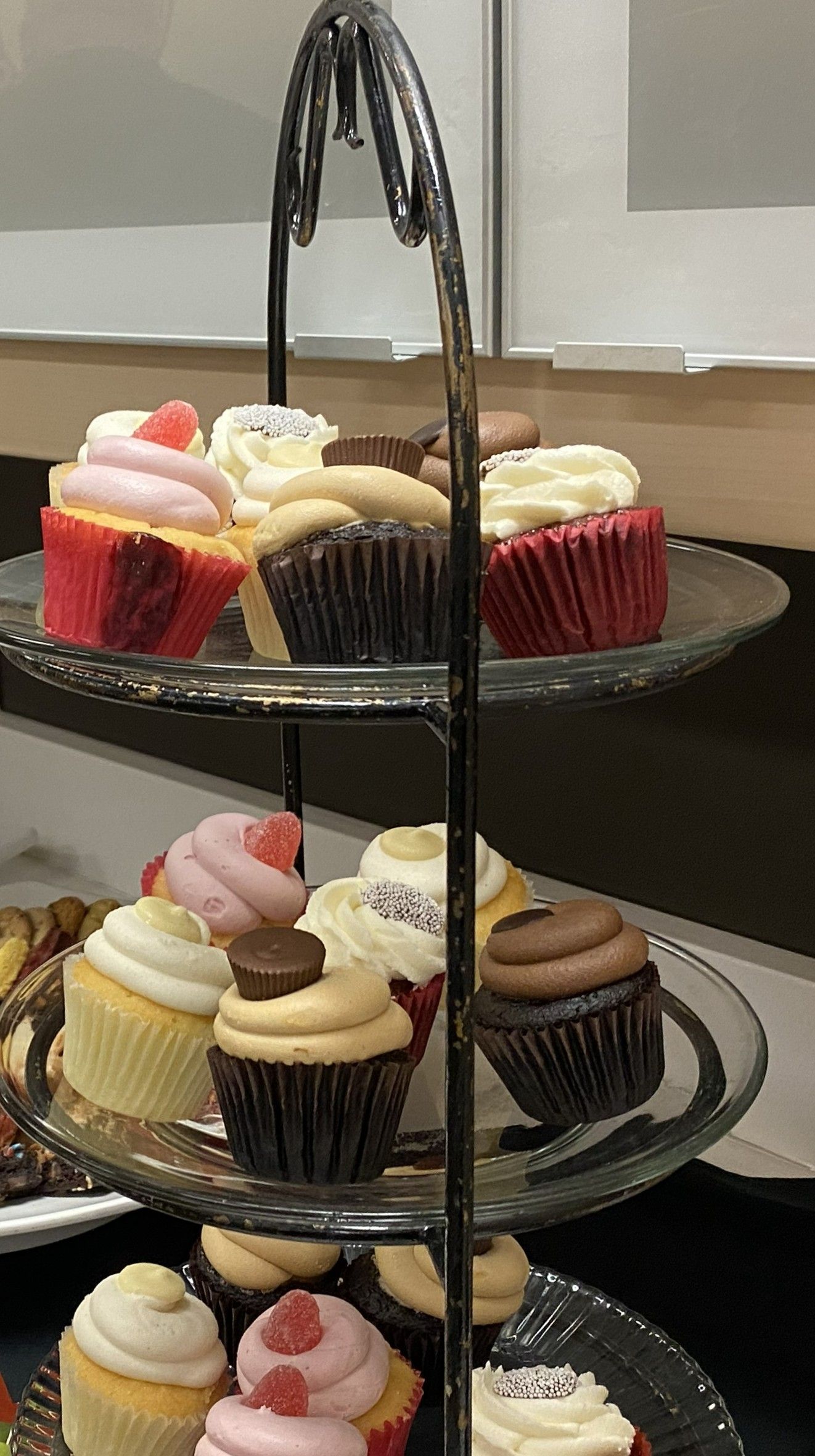 A tiered serving stand holding an assortment of decorated cupcakes with various frosting colors and toppings.