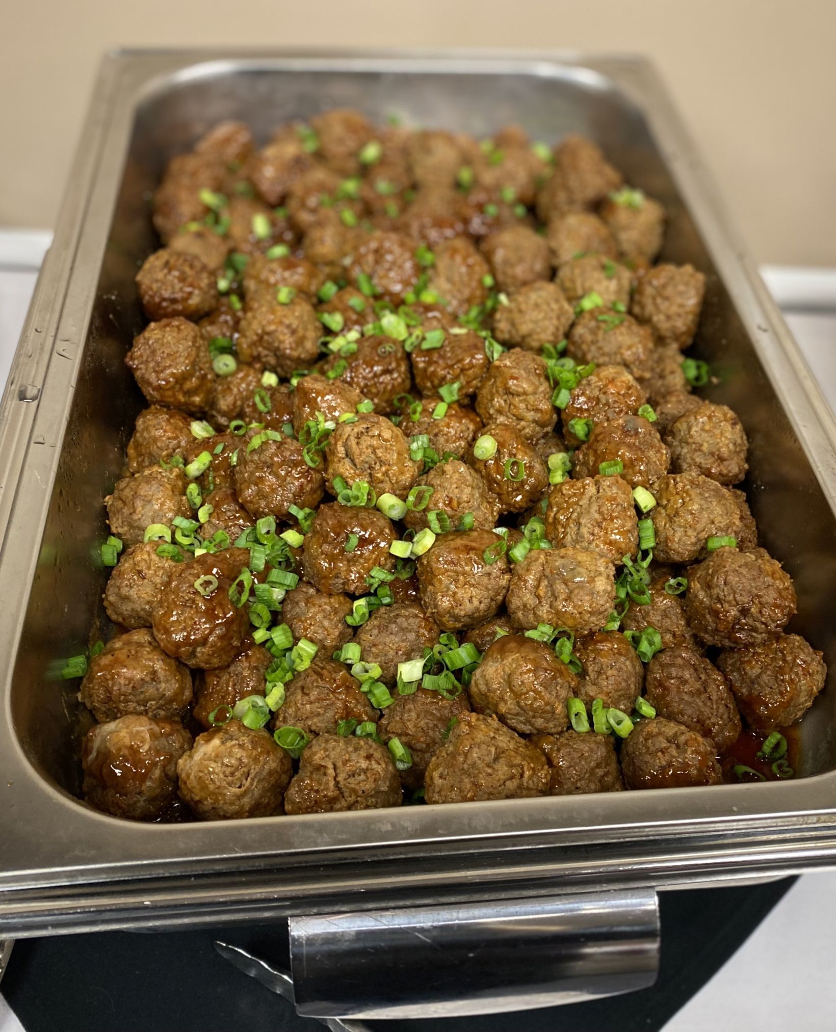 Tray of meatballs in sauce, garnished with green onions.