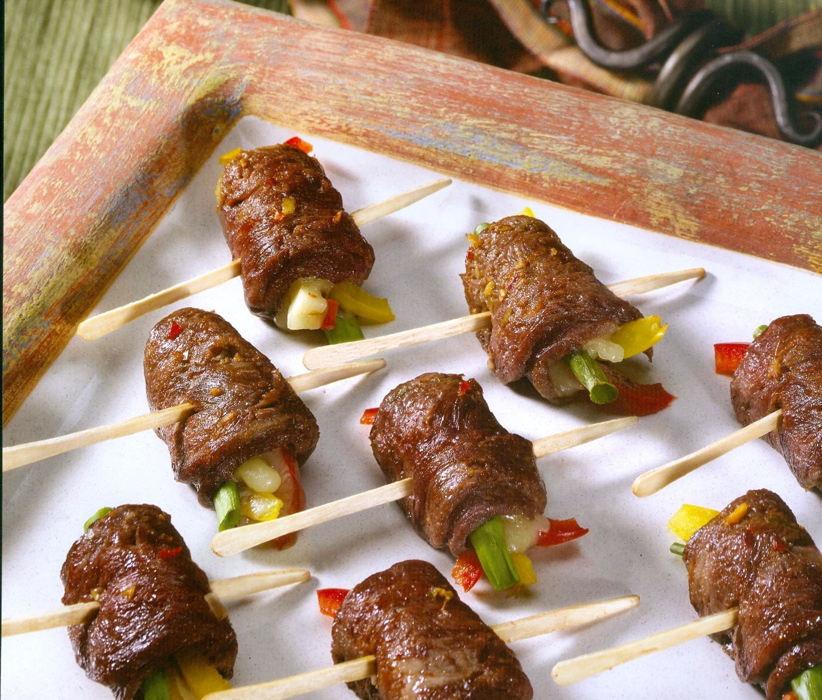 Beef rolls with colorful vegetables on toothpicks, arranged on a white surface.
