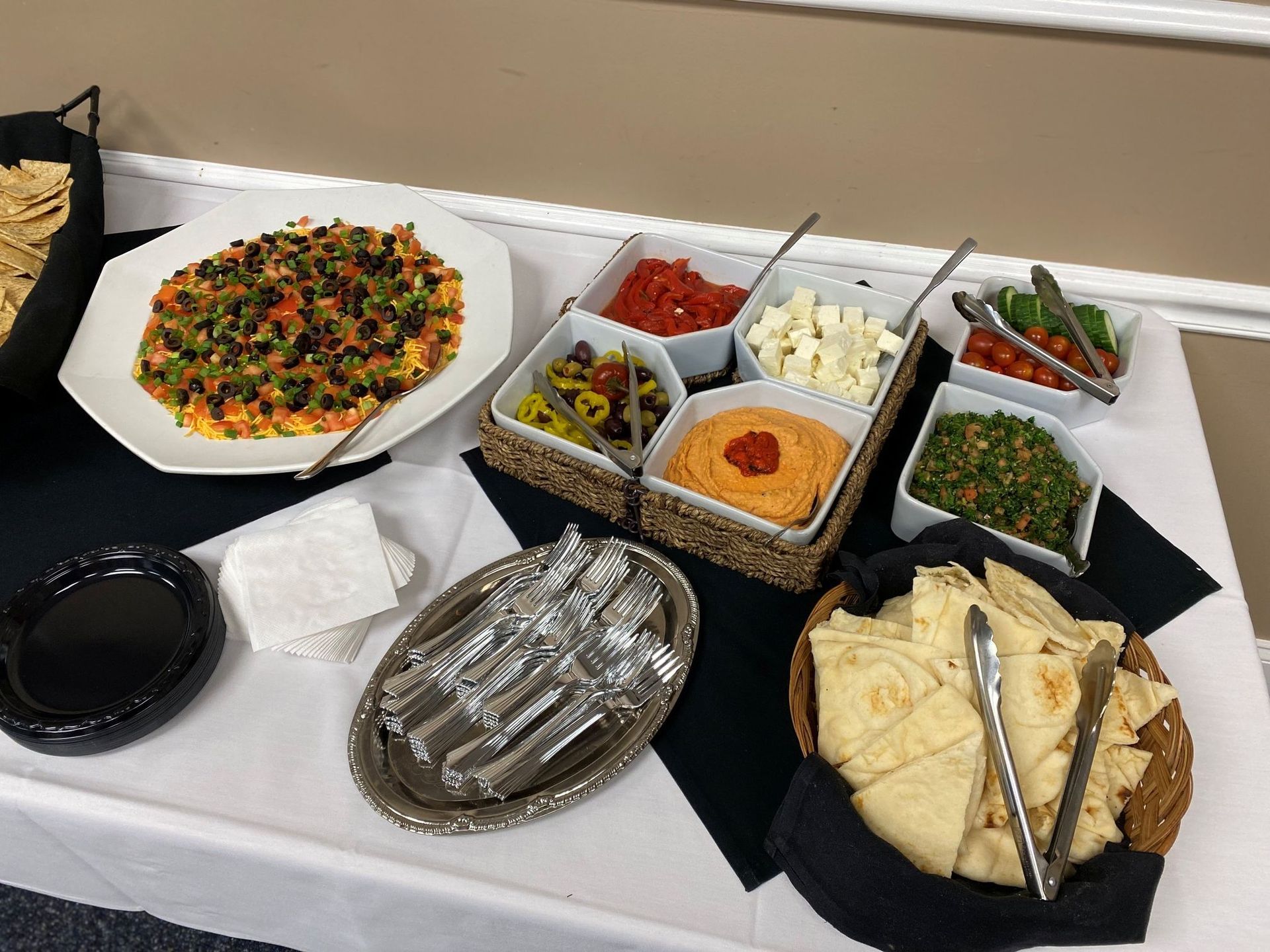 Buffet with Mediterranean dips, pita, and chips on a white tablecloth.