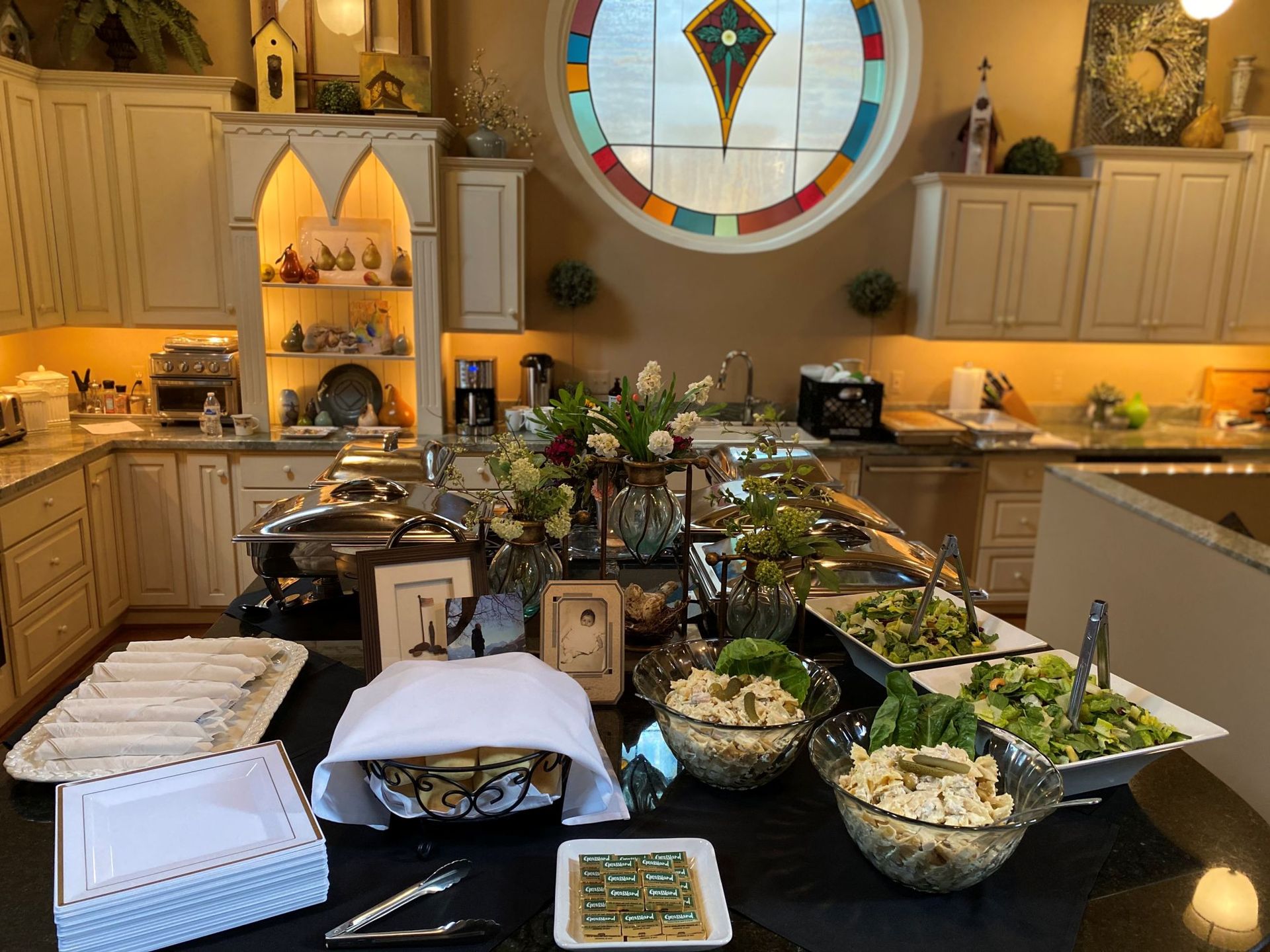 A buffet spread on a table in a kitchen with a stained-glass window.