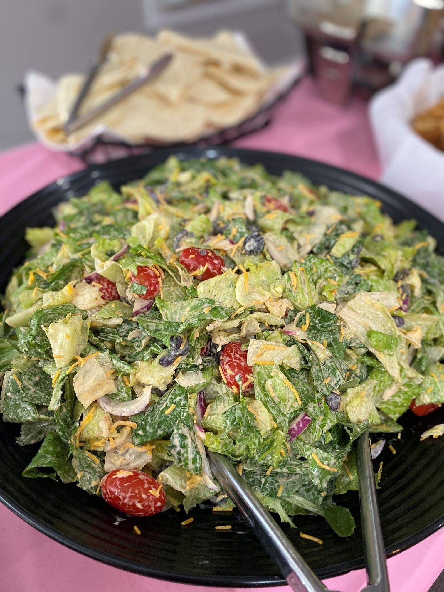 Salad in a black bowl with tomatoes and cheese, pink table.