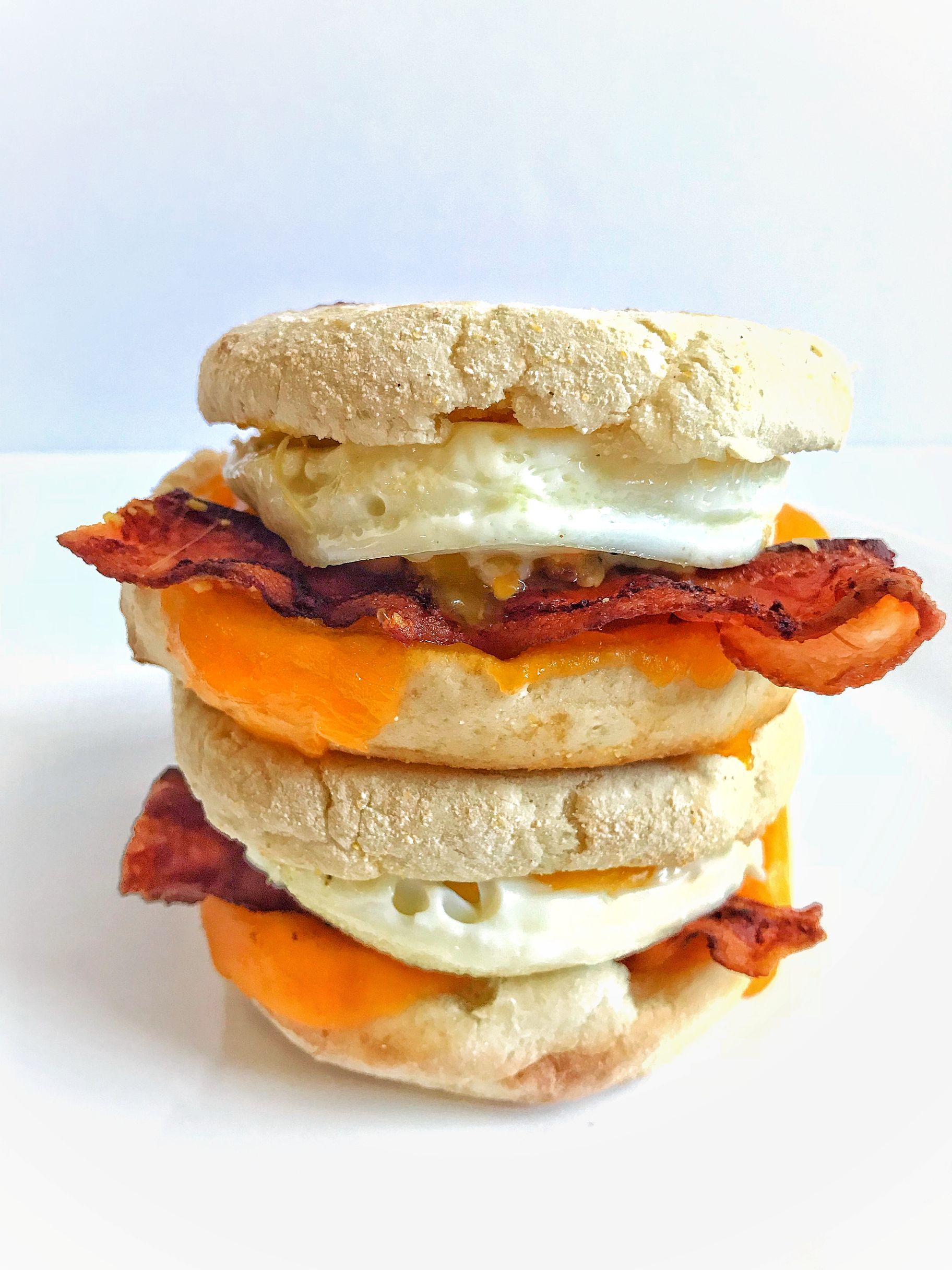 Breakfast sandwich on English muffins: eggs, bacon, cheese, stacked high.