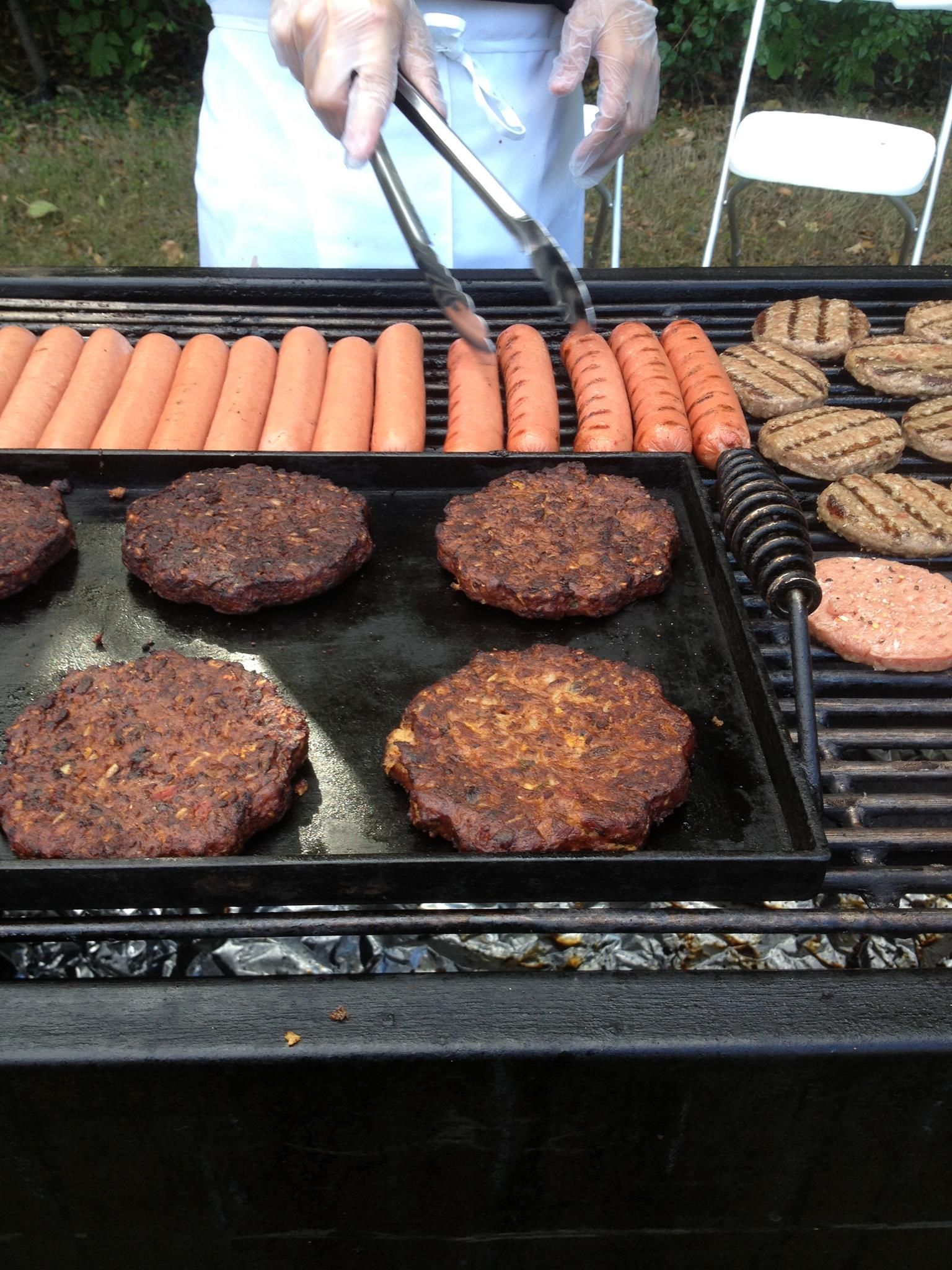 Burgers and hot dogs grilling on a barbecue, person using tongs.