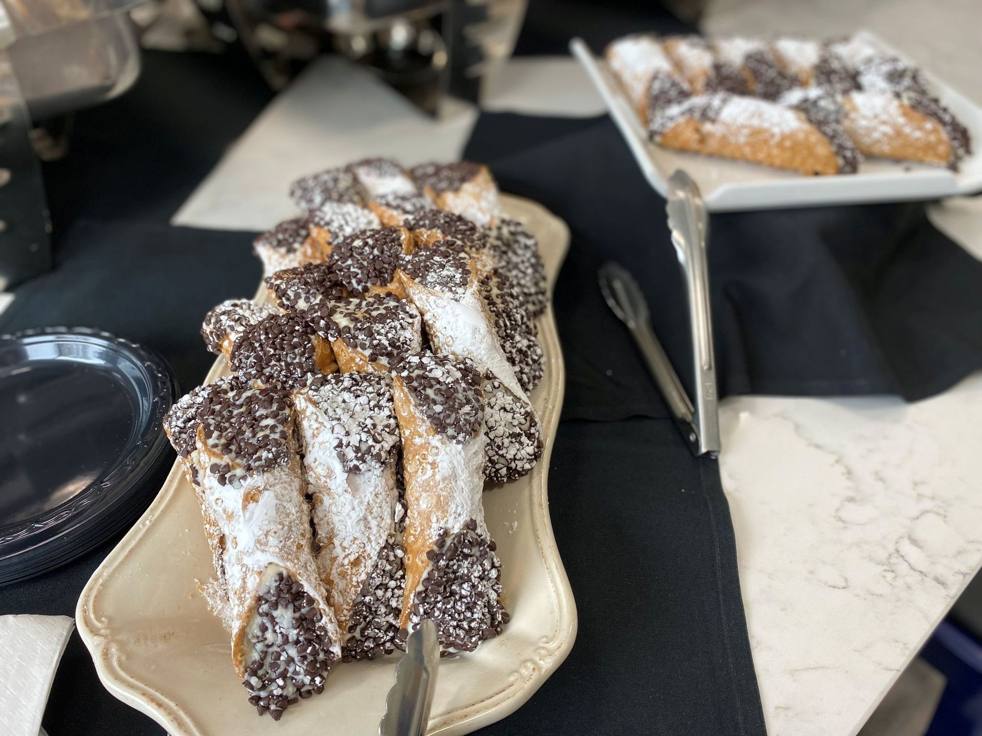 Cannoli pastries on a white platter, sprinkled with chocolate chips and powdered sugar.