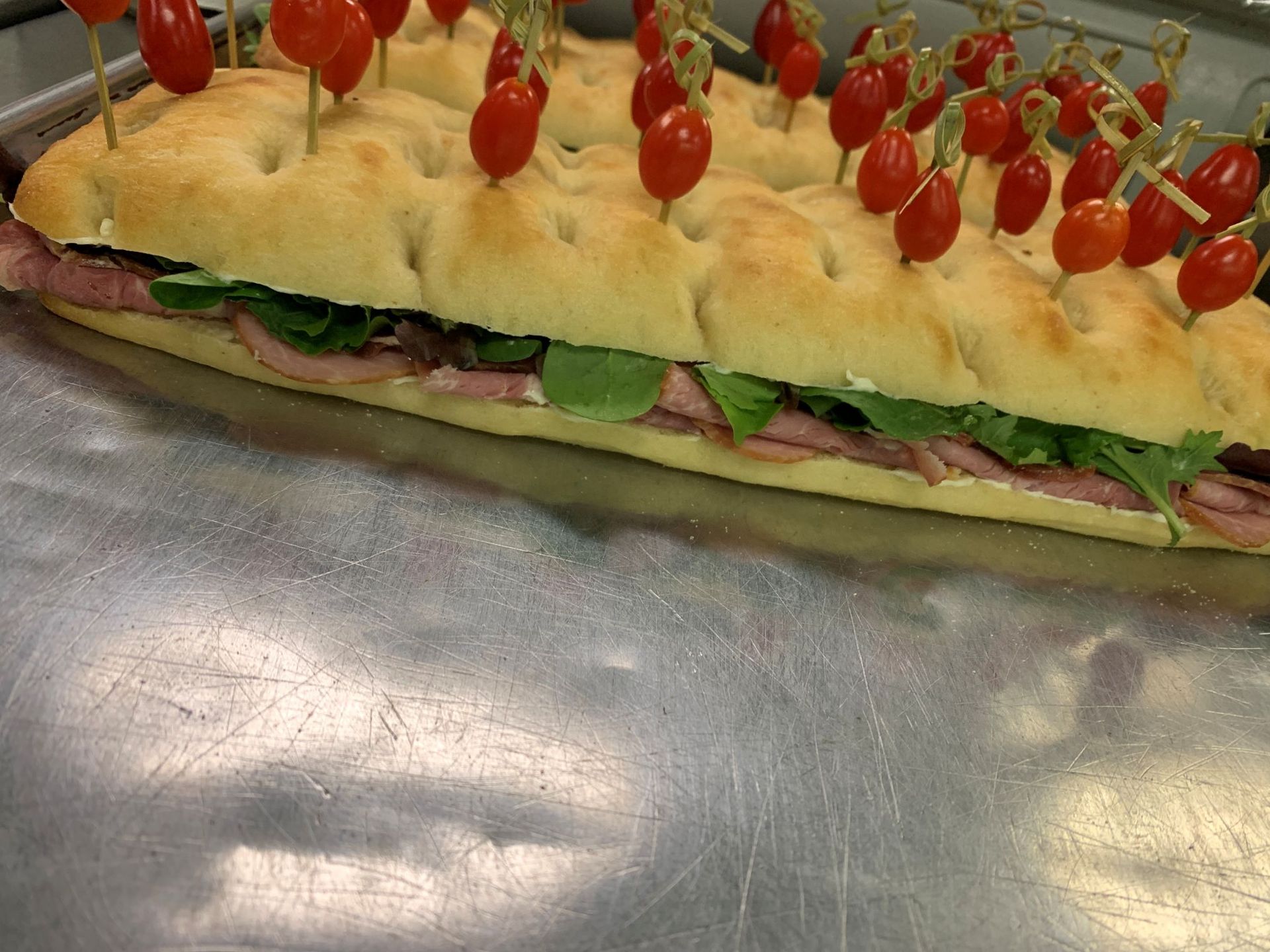 Large focaccia sandwich with tomato skewers on a metal tray.