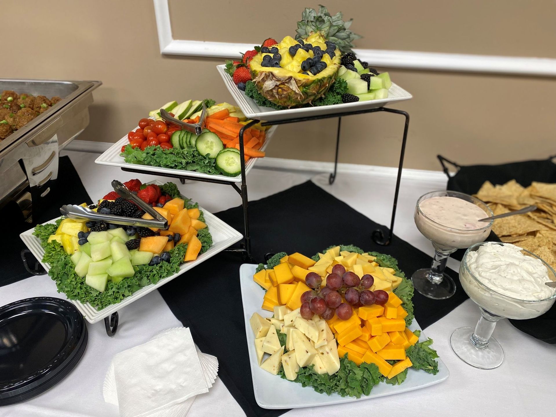 A buffet table with fruit, vegetables, cheese, dips, and chips.