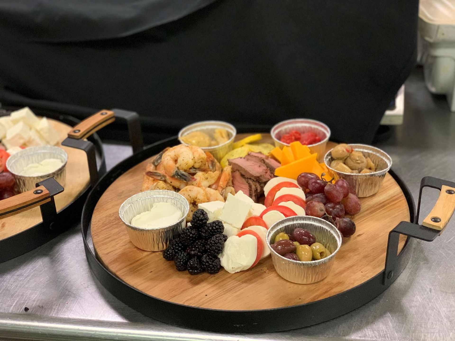 Wooden charcuterie board with assorted food: shrimp, cheese, fruits, nuts, olives, and dipping sauces.