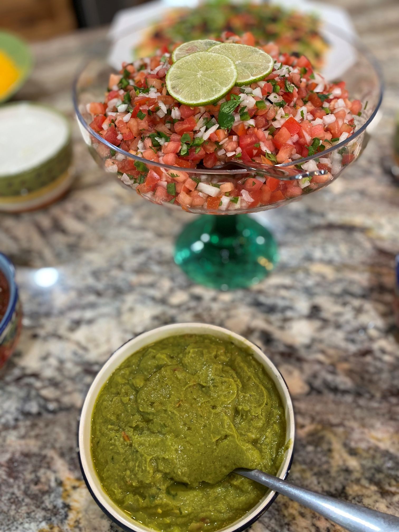A bowl of salsa and green sauce with garnishes on a countertop.