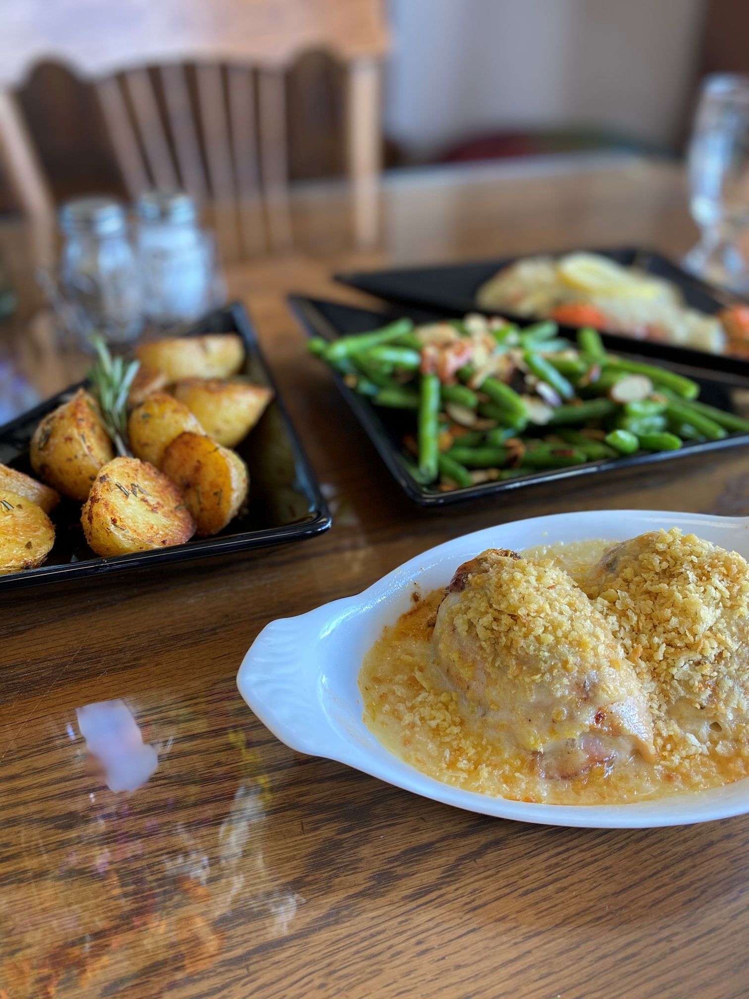 Chicken dish with breadcrumb topping, roasted potatoes, and green beans on a wooden table.