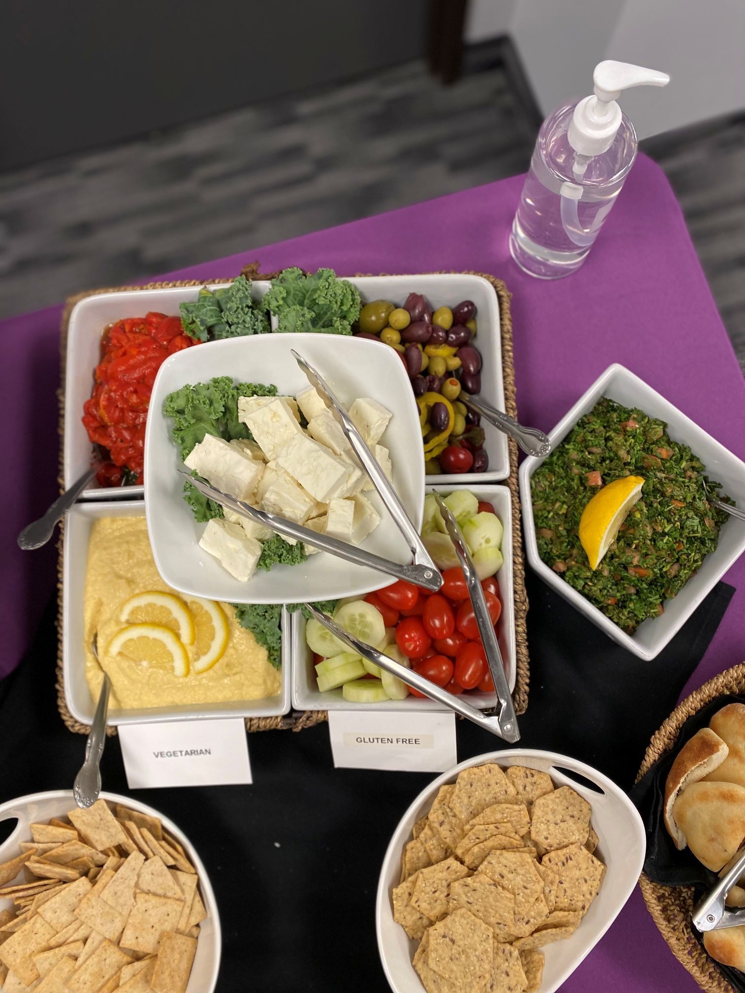 Appetizer platter with hummus, vegetables, olives, cheese, and crackers, beside hand sanitizer.
