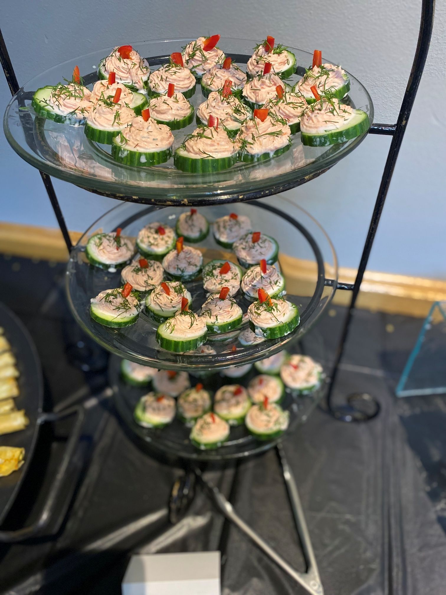 Cucumber appetizers with pink topping and dill on a tiered serving tray.